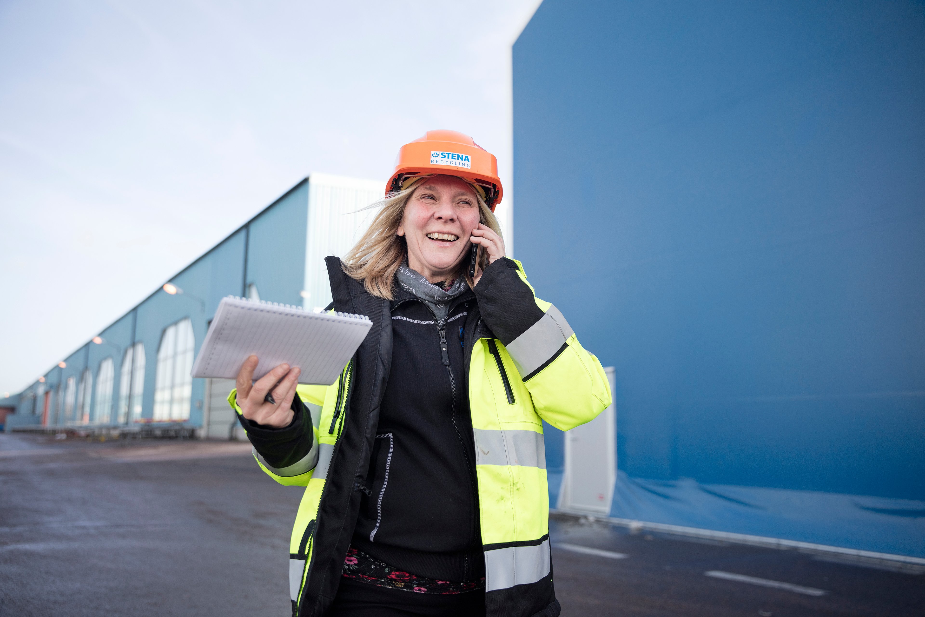 A smiling female Stena Recycling employee in protective clothing talks on her mobile phone