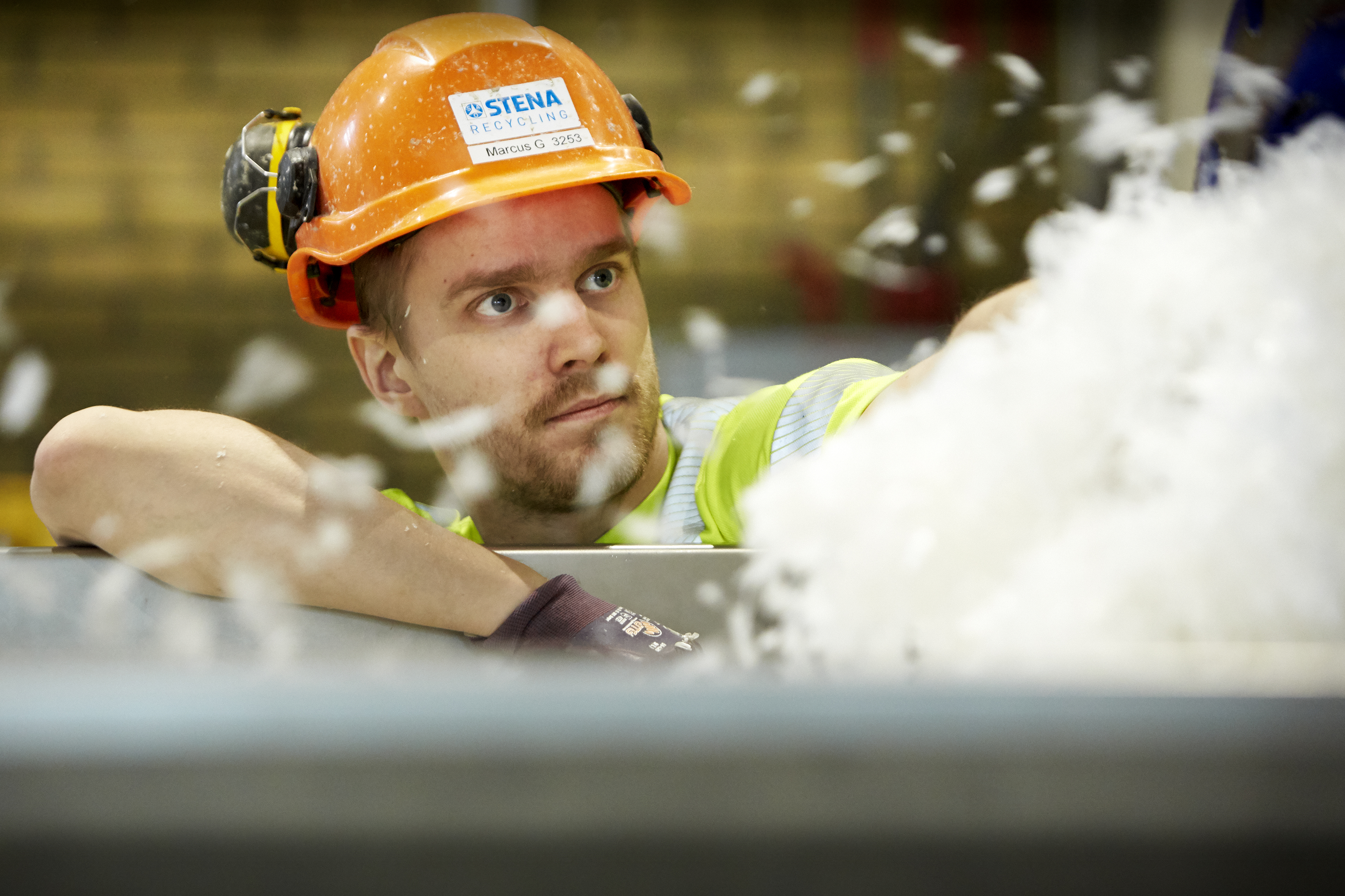 Ekspert ds recyklingu, w kasku z logo Stena Recycling sprawdzający kontener z plastikiem do recyklingu