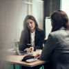 Three collegues sitting at a table, focused on their laptops, engaged in a professional discussion.